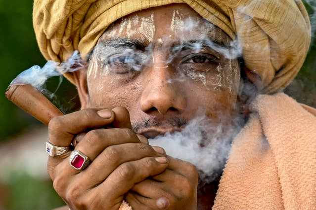 A kanwariya, devotee of the Hindu god Shiva, smokes with a traditional clay pipe as he rests along a road after collecting holy water from the river Ganges during the “Kanwar Yatra” pilgrimage in the sacred month of Sawan in New Delhi on July 21, 2025. (Photo by Money Sharma/AFP Photo)
