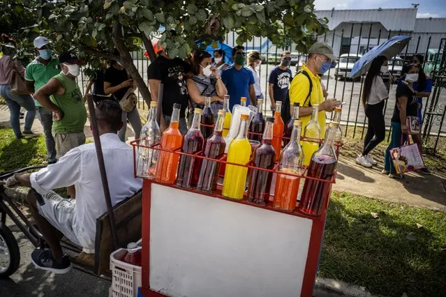 A snow cone vendor looks for customers amid a line of people, all wearing protective face masks as a precaution during the spread of the new coronavirus, waiting to enter a grocery store that accepts U.S. dollars in Havana, Cuba, Monday, July 20, 2020. Cuba has expanded the types of stores that accept dollars for payment to include food stores, as part of the government’s effort to capture much needed hard currency to shore up the island’s ailing economy. (Photo by Ramon Espinosa/AP Photo)