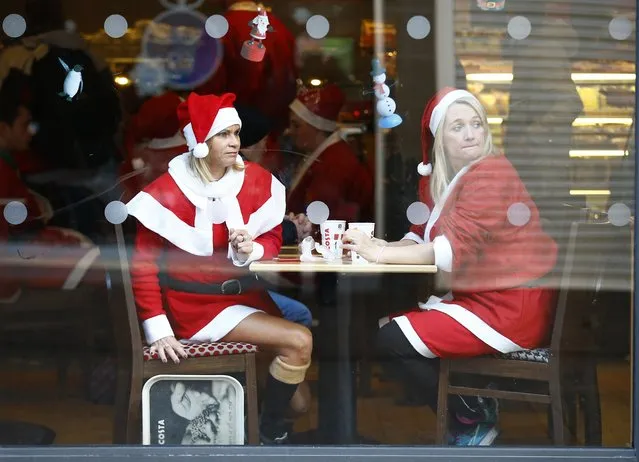 Competitors dressed in Santa costumes look from a coffee shop before an annual charity Santa fun run in Loughborough, central England, December 7, 2014. (Photo by Darren Staples/Reuters)