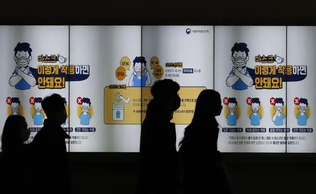 People wearing face masks walk past a screen showing the precautions against the coronavirus in Seoul, South Korea, Friday, November 20, 2020. The screen reads: “Don't wear such masks like below images”. (Photo by Lee Jin-man/AP Photo)