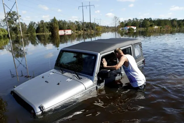 After coming across a Jeep surrounded by floodwaters associated with Hurricane Matthew,  Elmer McDonald inspects the interior to make certain nobody was inside as he makes his way through a strong current after checking on his own mobile home for the first time on Thursday, October 13, 2016, in Lumberton, N.C.  About 1,200 Lumberton residents had to be evacuated by boat and plucked from their roofs by helicopters as the river crested; McDonald was one of thousands who evacuated. (Photo by Brian Blanco/AP Photo)