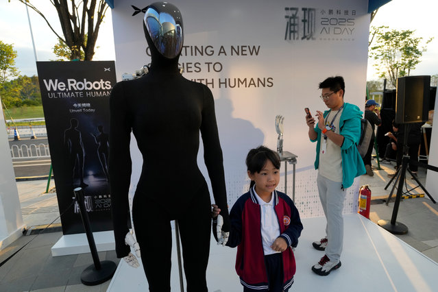 A child poses next to the newly unveiled XPENG next generation IRON robot during the XPENG AI Day held at the company headquarters in Guangzhou in southern China's Guangdong province, Wednesday, November 5, 2025. (Photo by Ng Han Guan/AP Photo)
