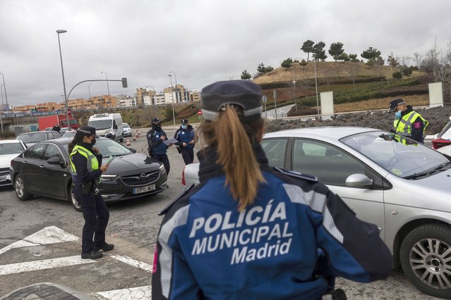 A police officer checks a driver's documents at a checkpoint on the outskirts of Madrid, Spain, Monday, January 25, 2021. With several regions reporting Friday new daily records of infections, some regional governments are toughening their response. The central Madrid region, home to 6.6 million, brought its curfew from midnight to 10 p.m. starting on Monday, and ordered shop, bar and restaurant closures at 9 p.m. the latest. (Photo by Bernat Armangue/AP Photo)