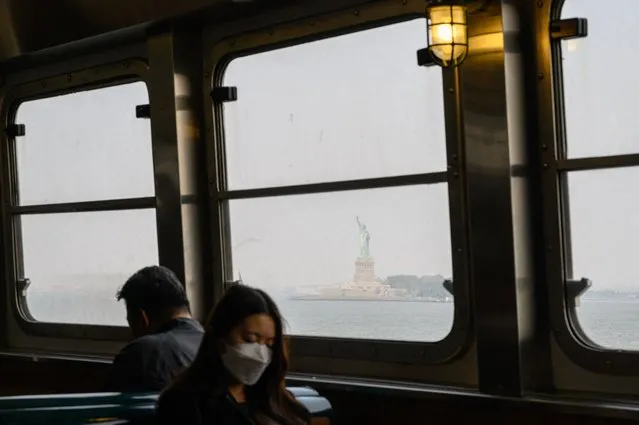 A passenger wearing a face mask rides the Staten Island Ferry past the Statue of Liberty during heavy smog in New York on June 6, 2023. Smoke from Canada's wildfires has engulfed the Northeast and Mid-Atlantic regions of the US, raising concerns over the harms of persistent poor air quality. (Photo by Ed Jones/AFP Photo)