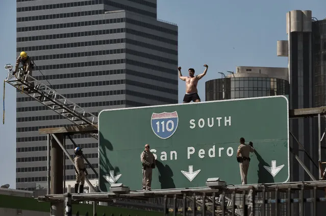 California Highway Patrol officers try to coax a man off a freeway sign in downtown Los Angeles, Wednesday, June 27, 2018. The man suspended banners, one about fighting pollution, after climbing onto the sign over State Route 110 during the Wednesday morning rush hour. (Photo by Richard Vogel/AP Photo)