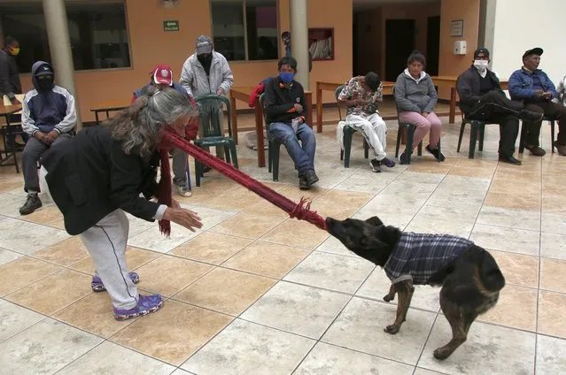 A woman plays with a dog as she waits for a free lunch provided by the Patronato San Jose shelter in Quito, Ecuador, Thursday, March 18, 2021, amid the new coronavirus pandemic. (Photo by Dolores Ochoa/AP Photo)