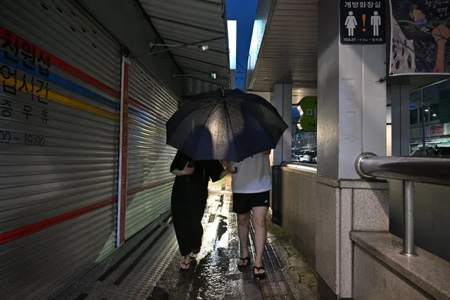 A couple share an umbrella as they walk along a pavement as it rains in the southeastern port city of Busan on August 9, 2023, the evening before the expected landfall of Typhoon Khanun on the country's southern coast. (Photo by Anthony Wallace/AFP Photo)