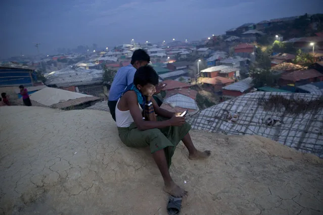 Rohingya Muslims use their cellphones as they sit on a hillock overlooking Balukhali refugee camp, in Bangladesh, Wednesday, November 14, 2018. Bangladesh authorities said they are ready to begin repatriating some of the more than 700,000 Rohingya Muslims who have fled from army-led violence in Myanmar since last year, but refugees scheduled to leave said they would refuse to go because of fears for their safety. (Photo by Dar Yasin/AP Photo)