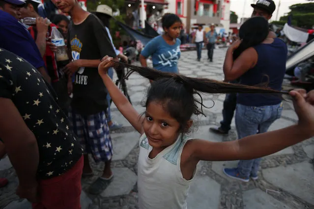 Seven-year-old Evelin Flores, from Honduras, plays with her hair as she stands in the plaza where her family is camping out in Tapanatepec, Oaxaca state, Mexico, Saturday, October 27, 2018, as the migrant caravan stops for the night. In the migrant caravan currently in southern Mexico, it's particularly tough for children and families who are trying to keep things together after more than two weeks on the road. (Photo by Rebecca Blackwell/AP Photo)
