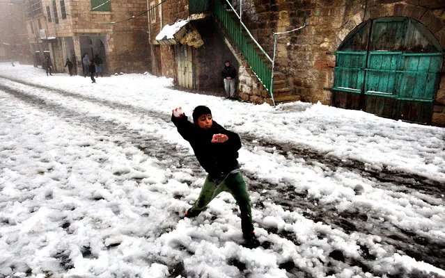 A Palestinian boys throws a snowball near Ibrahimi Mosque or the Tomb of the Patriarch, a religious site to both Muslims and Jew, in the West Bank town of Hebron as snow falls on December 12, 2013. A bruising winter storm brought severe weather to the Middle East, forcing the closure of roads and schools and blanketing much of the high altitude areas with snow and ice. (Photo by Hazem Bader/AFP Photo)