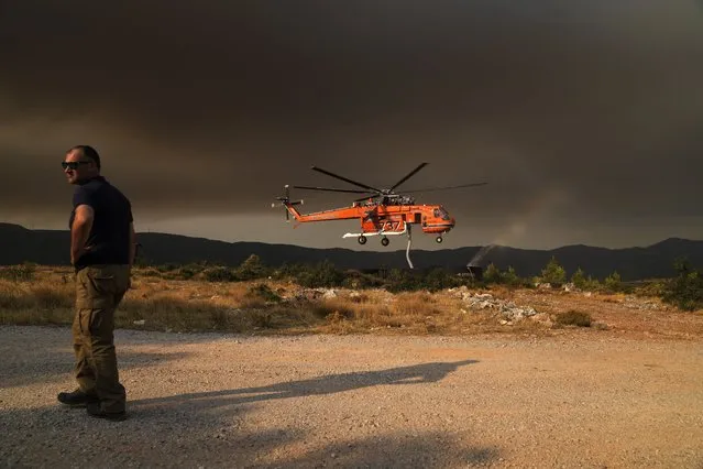An helicopter fills from a water tank during a wildfire near Vilia area some 60 kilometers (37 miles) northwest of Athens, Greece, Wednesday, August 18, 2021. A major wildfire northwest of the Greek capital devoured large tracts of pine forest for a third day and threatened a large village as hundreds of firefighters, assisted by water-dropping planes and helicopters, battled the flames Wednesday. (Photo by Thanassis Stavrakis/AP Photo)