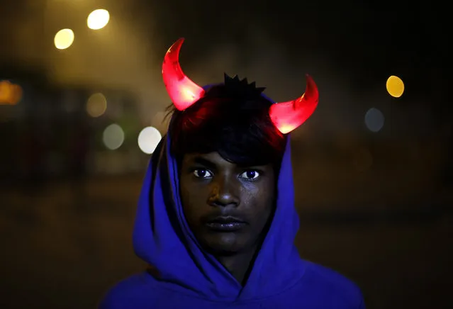 An Indian boy wearing an illuminated devil horns waits for customers as he sells Christmas merchandise, outside the Sacred Heart's Cathedral in New Delhi, India, Tuesday, December 24, 2013. (Photo by Altaf Qadri/AP Photo)