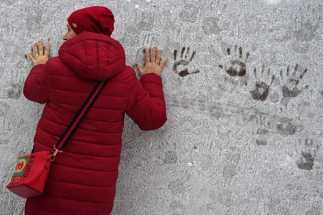 A woman leaves handprints on a frost-covered wall in St. Petersburg, Russia, Tuesday, January 9, 2024. Frost appeared on stone surfaces after warming that followed several days of severe frost. (Photo by Dmitri Lovetsky/AP Photo)
