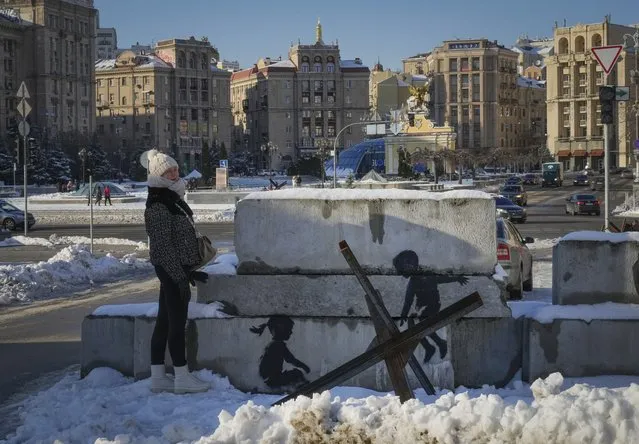 A woman stands next to a picture with an artwork on concrete blocks which were installed to protect the city from the Russian troops, in the main square in Kyiv, Ukraine, Thursday, December 1, 2022. The painting appears to have been made by British street artist Banksy, who confirmed this on his Instagram account. (Photo by Efrem Lukatsky/AP Photo)