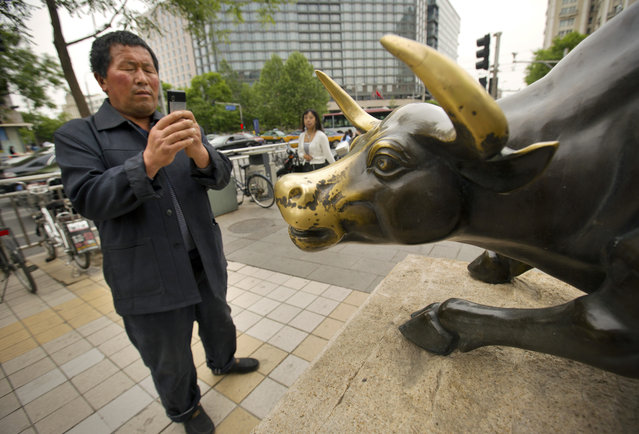 In this May 6, 2015 photo, a tourist from China's Inner Mongolia Province takes a photo of a statue of a bull in Beijing. After months of cheerleading for rising prices, China's leaders are trying to tap the brakes on a stock market boom that could run out of control and disrupt economic reform plans. (Photo by Mark Schiefelbein/AP Photo)