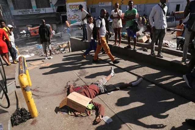 People walk past the body of a man who was shot dead earlier in the morning, amid an escalation in gang violence, in Port-au-Prince, Haiti, on March 18, 2024. (Photo by Ralph Tedy Erol/Reuters)