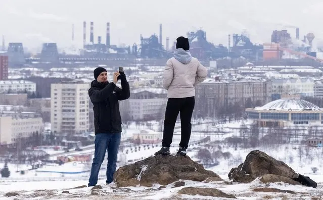 A man takes a picture of a woman with city centre and Nizhny Tagil metallurgical combinate NTMK owned by EVRAZ group in the background, in Nizhny Tagil, Russia on November 21, 2021. (Photo by Maxim Shemetov/Reuters)