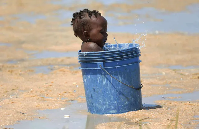 A baby plays with water in a bucket at a camp for displaced survivors of Cyclone Idai in Beira, Mozambique, Sunday, March, 31, 2019. Cholera cases among cyclone survivors in Mozambique have jumped to 271, authorities said. So far no cholera deaths have been confirmed, the report said. Another Lusa report said the death toll in central Mozambique from the cyclone that hit on March 14 had inched up to 501. Authorities have warned the toll is highly preliminary as flood waters recede and reveal more bodies. (Photo by Tsvangirayi Mukwazhi/AP Photo)