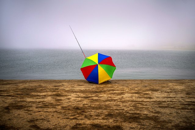 Francisco Claramunt, 73, uses an umbrella to shelter from the cold wind as he sits fishing on a breakwater on a foggy morning in Barcelona, Spain, Monday, March 18, 2024. (Photo by Emilio Morenatti/AP Photo)