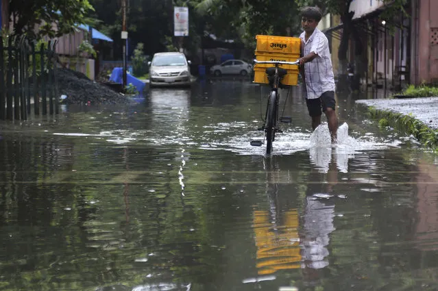 A man pushes his bicycle, carrying milk for sale, past a waterlogged street after rainfall in Mumbai, India, Wednesday, July 24, 2019. India's monsoon season runs from June to September. (Photo by Rafiq Maqbool/AP Photo)