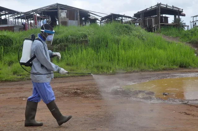 Ebola health workers spray disinfectant on a road near the home of a 17-year old boy that died from the Ebola virus on the outskirts of Monrovia, Liberia, Wednesday, July 1, 2015.  Liberian officials confirmed a second Ebola case Wednesday in the same town where the disease was detected days earlier from the corpse of a teenager, seven weeks after the country was declared Ebola-free.(Photo by Abbas Dulleh/AP Photo)