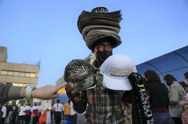A man sells hats with the name of Mexican singer Alejandro Fernandez and Colombian singer Jessi Uribe as people line up to get into the concert in Caracas, Venezuela, March 3, 2022. (Photo by Ariana Cubillos/AP Photo)