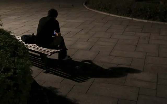 A man casts a shadow on the ground as he sits on a bench near a street light at night near the Atomic Bomb Dome in Hiroshima, western Japan July 27, 2015. (Photo by Issei Kato/Reuters)
