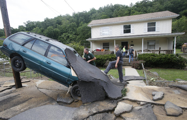 Jay Bennett, left, and step-son Easton Phillips survey the damage to a neighbors car in front of their home damaged by floodwaters as the cleanup begins from severe flooding in White Sulphur Springs, W. Va., Friday, June 24, 2016. (Photo by Steve Helber/AP Photo)