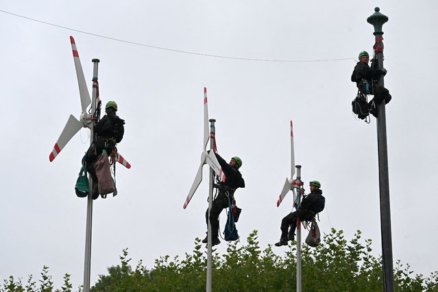 Greenpeace activists climb up flagpoles to fix mockups of wind turbines in front of the Bavarian State Chancellery in Munich, southern Germany, on August 30, 2023, as they call for more wind power. (Photo by Christof Stache/AFP Photo)