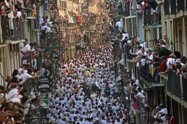 Revelers go on the way of the Estafeta street beside Fuente Ymbro fighting bulls as people look on from balconies during the first running of the bulls at the San Fermin Festival, in Pamplona, norther Spain, Thursday, July 7, 2016. Revelers from around the world arrive to Pamplona every year to take part in some of the eight days of the running of the bulls. (Photo by Alvaro Barrientos/AP Photo)