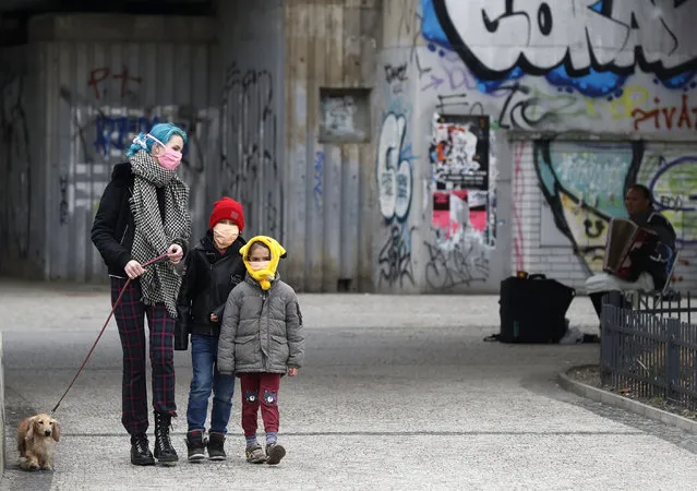 A woman with her children walk their dog in Prague, Czech Republic, Tuesday, March 17, 2020. Due to the outbreak of the novel coronavirus called COVID-19 the Czech capital banned all passengers from the public transport who would not have any face protection. The order by Prague's mayor Zdenek Hrib says the protection might include face masks, respirators or scarves will also do. (Photo by Petr David Josek/AP Photo)