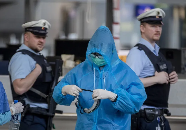A Chinese tourist prepares for his flight to China as two German police officers walk by at the airport in Frankfurt, Germany, Sunday, March 29, 2020. Due to the coronavirus only a few flights are leaving the airport these days. (Photo by Michael Probst/AP Photo)