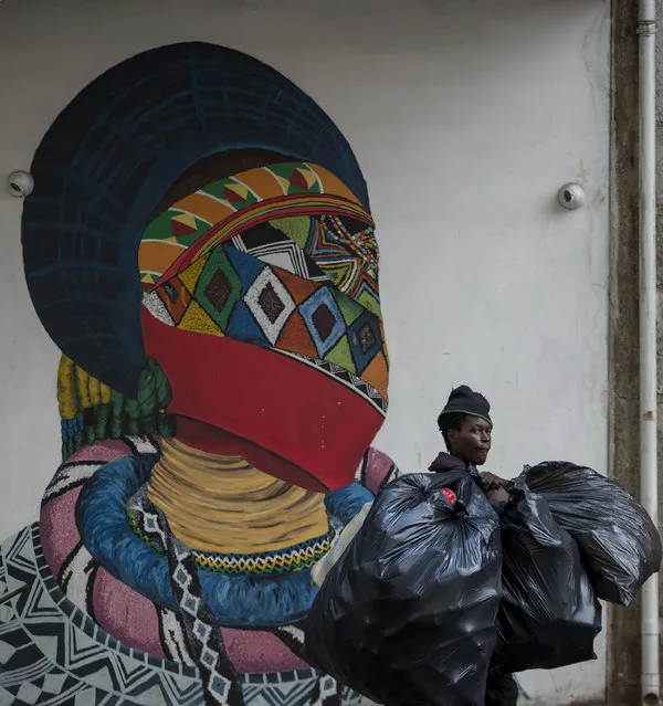 A man carrying plastic bags walks past a mural outside the Wits University school of art in Johannesburg, South Africa, Monday, March 16, 2020. South African President Cyril Ramaphosa declared a national state of disaster. Ramaphosa said all schools will be closed for 30 days from Wednesday and he banned all public gatherings of more than 100 people. South Africa will close 35 of its 53 land borders and will intensify screening at its international airports. For most people, the new COVID-19 coronavirus causes only mild or moderate symptoms. For some it can cause more severe illness. (Photo by Themba Hadebe/AP Photo)