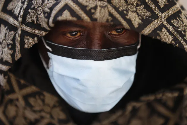 A man wears a protective mask while waiting for a bus in Detroit, Wednesday, April 8, 2020. Detroit buses will have surgical masks available to riders starting Wednesday, a new precaution the city is taking from the new coronavirus COVID-19. (Photo by Paul Sancya/AP Photo)