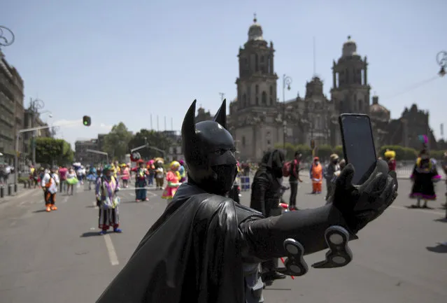 A street performer dressed as Batman takes a selfie during a protest in Mexico City, Thursday, April 30, 2020. The city's street performers marched to Mexico City’s main square the Zocalo, protesting in front of the national palace against restrictions designed to help stop the spread of COVID-19 disease, barring them from working on the streets. (Photo by Fernando Llano/AP Photo)