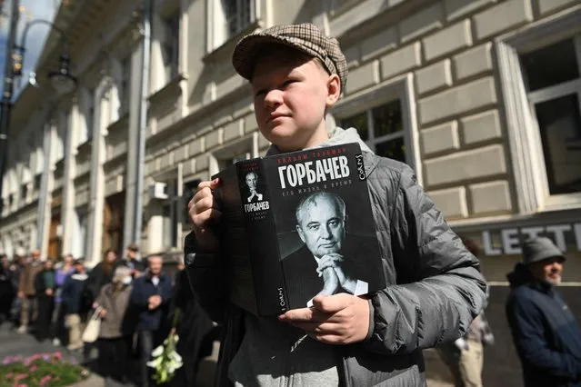 A man holds a book with Mikhail Gorbachev portrait as he stands in line to attend a farewell ceremony in front of the building of the Hall of Columns, where a farewell ceremony for the last leader of the Soviet Union and winner of the Nobel Peace Prize in 1990, Mikhail Gorbachev is taking place in Moscow on September 3, 2022. Last Soviet leader Mikhail Gorbachev will be laid to rest Saturday in a Moscow ceremony, but without the fanfare of a state funeral and with the glaring absence of President Vladimir Putin. (Photo by Natalia Kolesnikova/AFP Photo)
