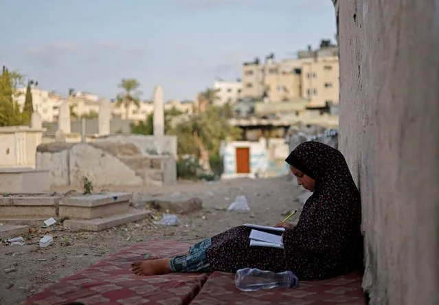 Lamis Kuhail, 12, studies for school in the Sheikh Shaban cemetery where she lives with her family, in Gaza City, September 4, 2022.The children, who earn small amounts bringing water to funeral ceremonies, keep asking their parents when they will be able to move away from the cemetery. “I sometimes get invited by friends from school, but I can't invite them here, I am too shy to do that”, said Lamis. (Photo by Mohammed Salem/Reuters)