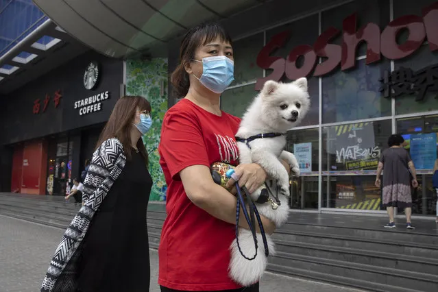 A woman wearing a mask to curb the spread of the coronavirus holds her dog as they pass by a mall in Beijing on Monday, June 29, 2020. (Photo by Ng Han Guan/AP Photo)