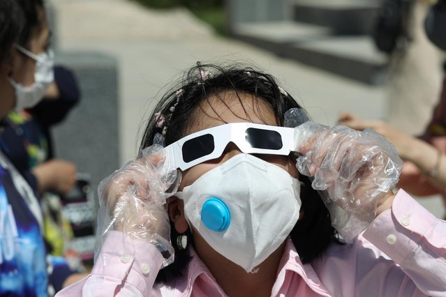 An Iranian girl wearing a protective face mask uses special protective glasses to observe a solar eclipse, in Tehran, Iran, June 21, 2020. (Photo by Ali Khara/WANA (West Asia News Agency) via Reuters)