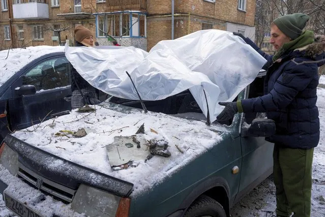 A couple cover their damaged car with a plastic tarp after a Russian attack in Kyiv, Ukraine, Wednesday, December 14, 2022. (Photo by Evgeniy Maloletka/AP Photo)