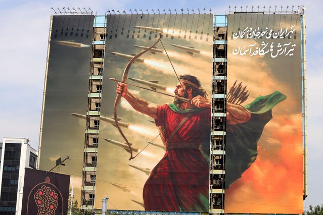 A picture taken on July 16, 2025 in Tehran's Vanak Square shows a recently unveiled billboard bearing an image featuring the legendary mythical Persian archer, Arash, with an excerpt from a poem in Farsi that reads: “For Iran, I place my soul in the bow. The arrow of Arash breaks through the sky”. The modern poetic composition is inspired by the legendary story of Arash the Archer, a mythical Iranian hero who appears in Persian literature, representing a nationalist and symbolic tale of self-sacrifice. (Photo by Atta Kenare/AFP Photo)