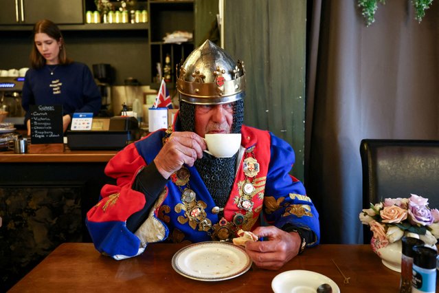 Mark Colyer, dressed as King John, takes a coffee and a bacon sandwich at a cafe during the Sweeps Festival in Rochester, Britain on May 6, 2024. (Photo by Kevin Coombs/Reuters)