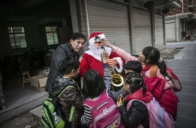 A worker holding a newly made Santa Claus model is surrounded by students in Yiwu, Zhejiang province December 4, 2014. (Photo by Reuters/China Daily)