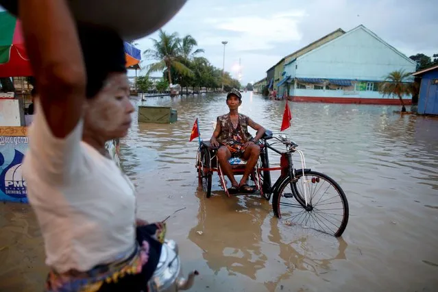 A man sits on his cart which he attached with National League for Democracy (NLD) party flags along a flooded street in Yangon in this September 30, 2015 file photo. (Photo by Soe Zeya Tun/Reuters)