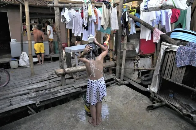 A girl takes a bath near a manual water pump at a slum area in Muntinlupa, Philippines, March 21, 2023. (Photo by Aaron Favila/AP Photo)