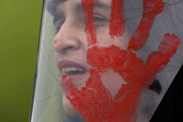 A demonstrator wears a face shield with a red handprint, mimicking blood, to protest Brazilian President Jair Bolsonaro's handling of the deadly coronavirus pandemic in Brasilia, Brazil, Wednesday, December 23, 2020. Protesters also called for the immediate start of COVID-19 vaccinations. (Photo by Eraldo Peres/AP Photo)