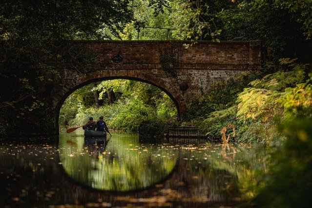 Luke Evans and Tom Pennicott paddle a canoe beneath Baseley's Bridge spanning the Basingstoke Canal, near Odiham, west of London, on October 7, 2025. The Basingstoke Canal was completed in 1794, built to connect Basingstoke with the River Thames at Weybridge. its intended purpose was to allow boats to travel from the docks in East London to Basingstoke. It was never a commercial success and around 1950, a lack of maintenance allowed the canal to become increasingly derelict. Restoration commenced in 1977 and on 10 May 1991 the canal was reopened as a fully navigable waterway. (Photo by Adrian Dennis/AFP Photo)