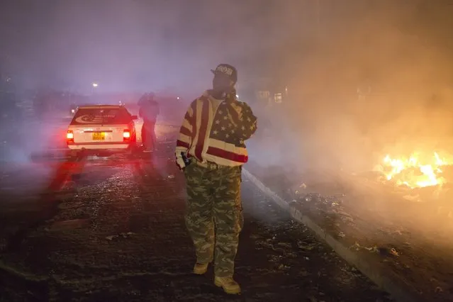 George Kiru, 36, walks past burning rubbish in Dandora, Nairobi, Kenya, June 14, 2015. Personally I always said no to crime, says Kiru, who buys and sells second-hand goods and picks up occasional work as a minibus driver to feed his two daughters and send them to school. "It never ends well if you choose to become a criminal. Eventually, you will get killed". (Photo by Siegfried Modola/Reuters)