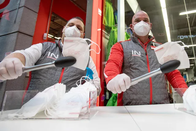 Employees of a supermarket use tongs to distribute FFP2 protective face masks to customers in Vienna on January 25, 2021, during the ongoing novel coronavirus (Covid-19) pandemic. Austria has decided to impose from January 25 a social distancing rule of two meters between each person in public places, instead of one meter until now. Wearing FFP2 masks will now also be compulsory in stores and on public transport. (Photo by Alex Halada/AFP Photo)