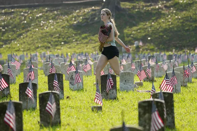 Liney Miles, 17, of Vicksburg, Miss., carrying a set of American flags, walks past the graves of American servicemen, many who are unknown, in the Vicksburg National Cemetery, Friday, May 26, 2023, in Vicksburg, Miss. About 18,000 flags are planted at each grave marker in advance of the Memorial Day weekend. (Photo by Rogelio V. Solis/AP Photo)